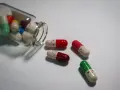 Kolorowe kapsułki, w tym leki psychotropowe, wysypują się ze szklanej buteleczki. Niektóre mają narysowane uśmiechnięte buźki.