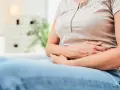 Kobieta siedzi na kanapie, trzymając się za brzuch. Częste gazy mogą być objawem raka, dlatego warto zwrócić uwagę na swoje ciało.