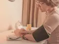Kobieta w okularach mierzy ciśnienie. Na stole leżą tabletki i budzik. To część jej codziennej rutyny, by dbać o tezeo.
