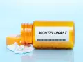 Pomarańczowa butelka leku Montelukast z białymi tabletkami na jasnoniebieskim tle.