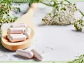 Kapsułki z kwasem kaprylowym na drewnianej łyżce, otoczone delikatnymi kwiatami i zielonymi gałązkami. Naturalne wsparcie dla zdrowia.