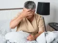 Kobieta w łóżku z ręką na czole, cierpiąca z powodu silnego bólu głowy.
