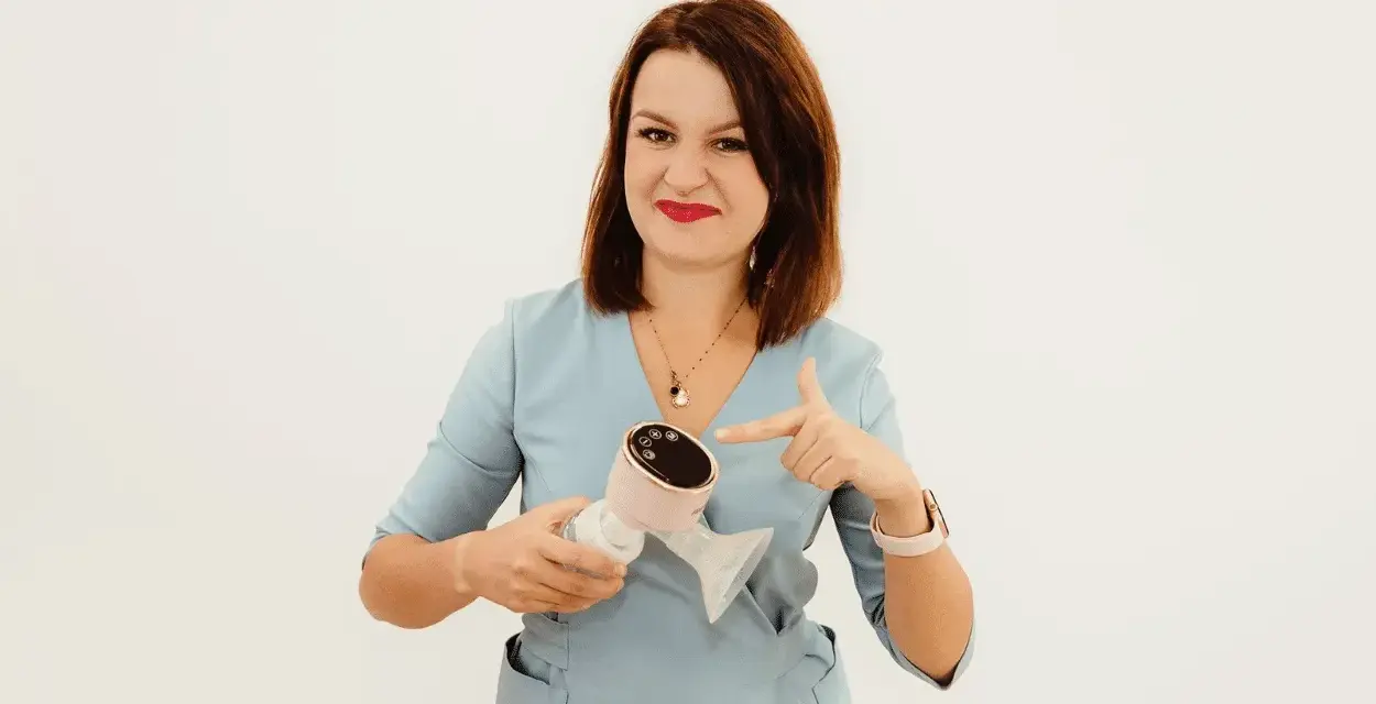 Kobieta w niebieskiej bluzce wskazuje palcem na różowy laktator elektryczny.