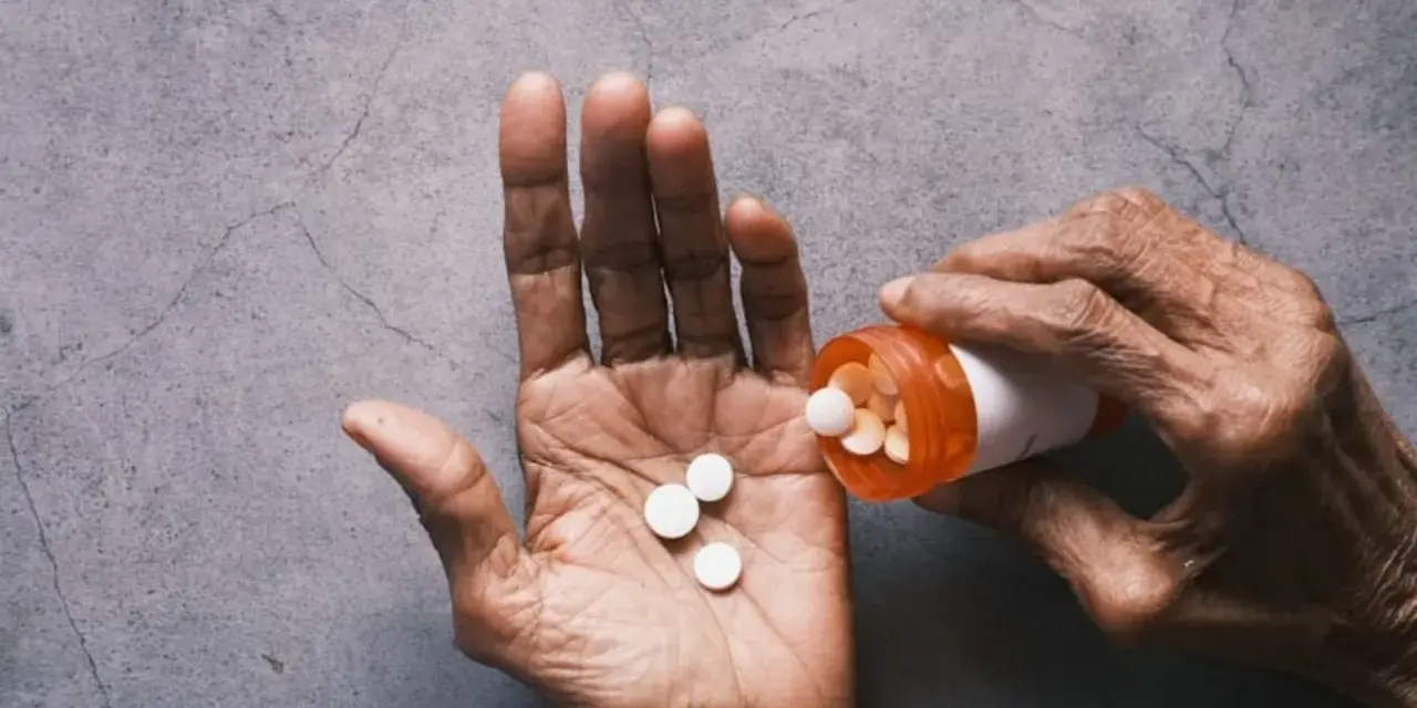 Dłoń wysypuje tabletki Tylenol z pomarańczowej buteleczki.