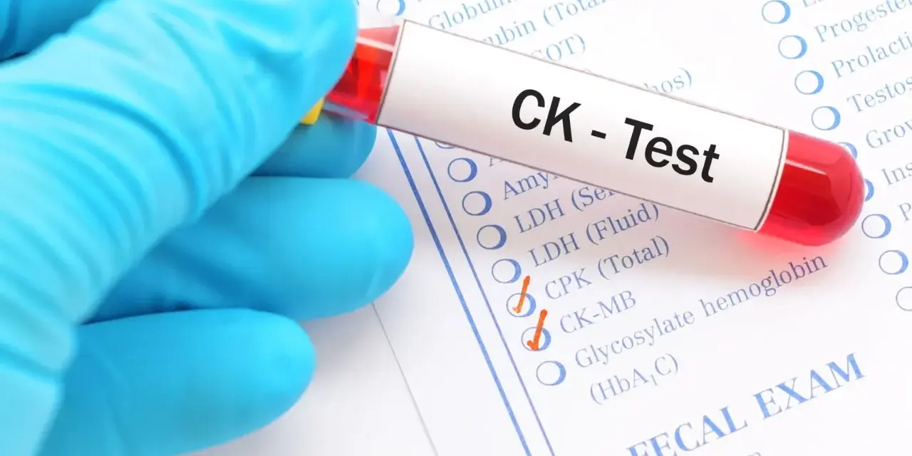 Ręka w niebieskiej rękawiczce trzyma probówkę z krwią do testu CK. Na formularzu zaznaczono CK-MB, co może wskazywać na badanie kinazy kreatynowej.