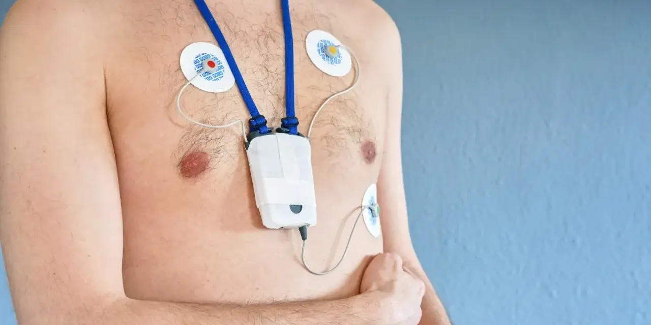 Mężczyzna z przyklejonymi elektrodami i urządzeniem holter ekg na szyi, monitorującym pracę serca.