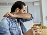 Mężczyzna zakrywa usta łokciem, trzymając kubek. Niepokojące objawy raka mogą się objawiać w różny sposób.