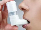 Dłoń trzyma biały inhalator, zbliżając go do ust osoby. To pomoc w oddychaniu, jak Ventolin aerozol.