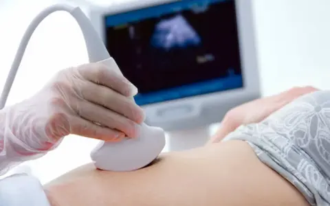 Dłoń w rękawiczce trzyma sondę USG na brzuchu, na ekranie widoczny obraz.