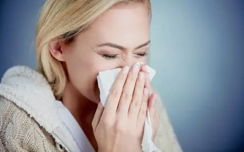 Kobieta z blond włosami chusteczką wyciera nos, cierpiąc na objawy alergii na pyłki.