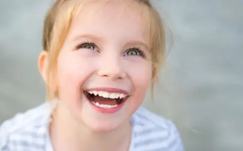 Uśmiechnięta dziewczynka z blond włosami, której radość przypomina o sile ducha w walce z zespołem Angelmana.