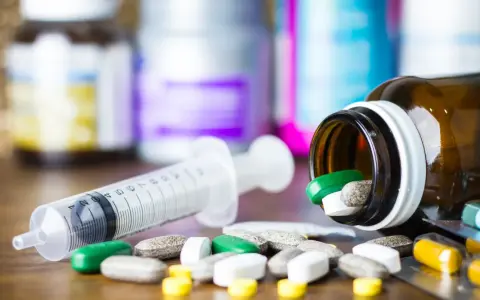 Leki, w tym zielone tabletki, rozsypane obok strzykawki i buteleczki. Może to być methocarbamol.