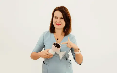 Kobieta w niebieskiej bluzce wskazuje palcem na różowy laktator elektryczny.