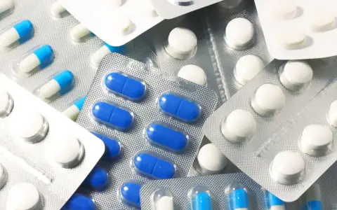 Blistry z białymi i niebiesko-białymi kapsułkami oraz białe tabletki. Wśród nich można znaleźć polopirynę, która pomaga złagodzić ból i gorączkę.