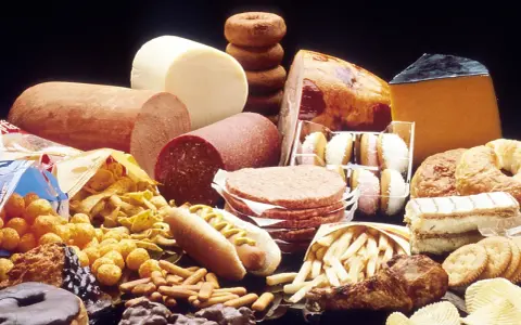 Stół ugina się pod ciężarem przetworzonej żywności: wędliny, sery, frytki, słodycze, ciastka, pączki, hamburgery i chipsy – to wszystko zawiera tłuszcze trans.
