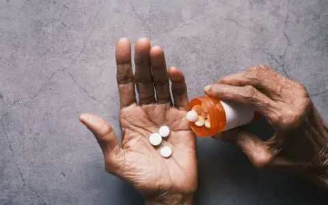 Dłoń wysypuje tabletki Tylenol z pomarańczowej buteleczki.