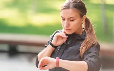 Kobieta w sportowej kurtce sprawdza na zegarku swój niski puls po treningu.