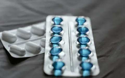 Dwa blistry leków: jeden z białymi kapsułkami, drugi z niebieskimi, które mogą być pregabalin sandoz.