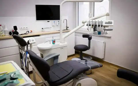 Nowoczesny gabinet stomatologiczny z fotelem, unitem i ekranem.