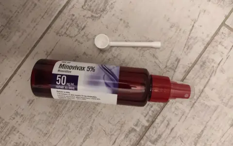 Butelka Minovivax 5% z aplikatorem na drewnianym tle.