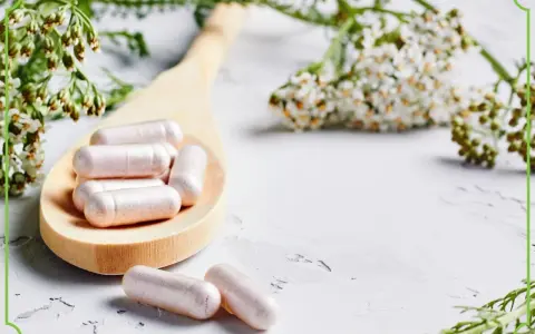 Kapsułki z kwasem kaprylowym na drewnianej łyżce, otoczone delikatnymi kwiatami i zielonymi gałązkami. Naturalne wsparcie dla zdrowia.