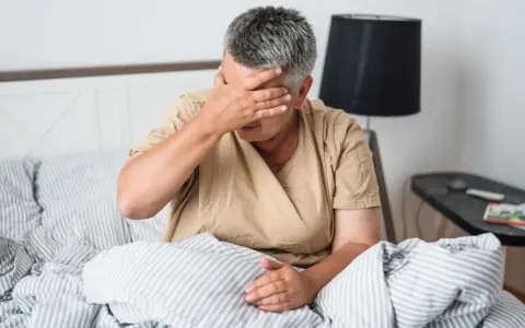 Kobieta w łóżku z ręką na czole, cierpiąca z powodu silnego bólu głowy.