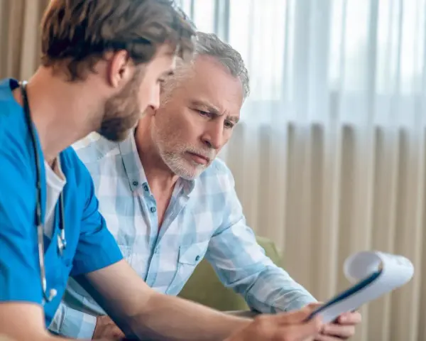 Lekarz w niebieskim fartuchu omawia z pacjentem wyniki badań, prawdopodobnie dotyczące biopsji prostaty.