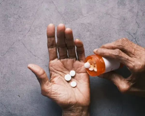 Dłoń wysypuje tabletki Tylenol z pomarańczowej buteleczki.