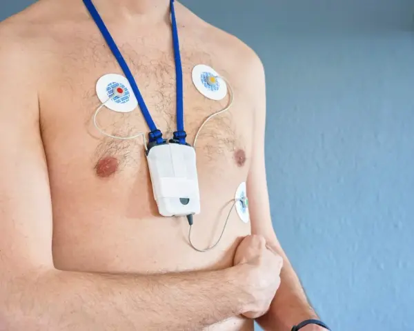 Mężczyzna z przyklejonymi elektrodami i urządzeniem holter ekg na szyi, monitorującym pracę serca.