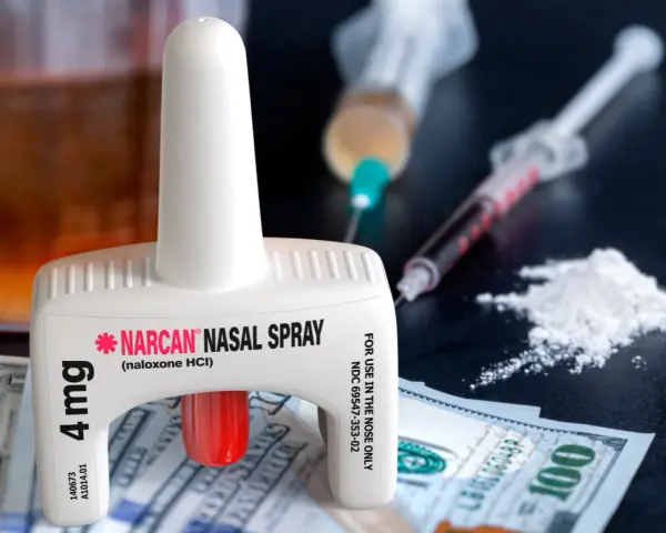 Nasalny spray nalokson, strzykawki z substancją, biały proszek i banknoty dolarowe.