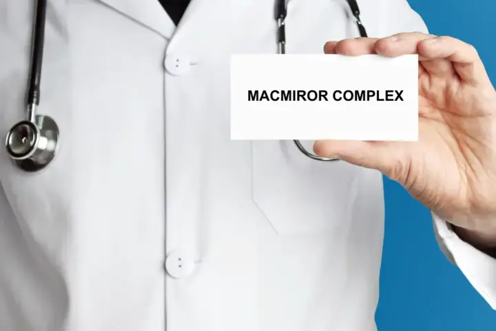 Lekarz w białym kitlu prezentuje kartkę z napisem MACMIROR COMPLEX. Stetoskop wisi na jego szyi.