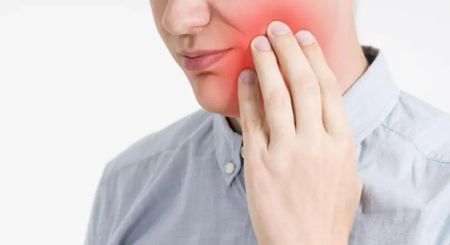 Mężczyzna trzyma się za policzek, gdzie widoczny jest czerwony obszar bólu. Może to być objaw zapalenia, np. davercin.