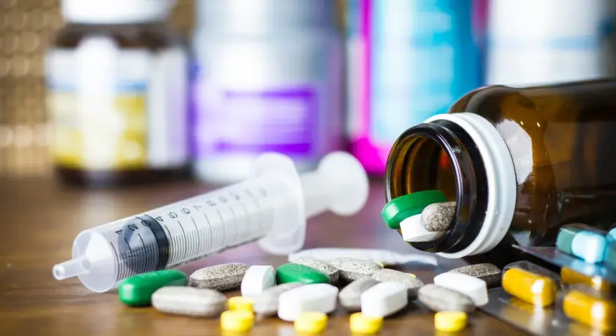 Leki, w tym zielone tabletki, rozsypane obok strzykawki i buteleczki. Może to być methocarbamol.