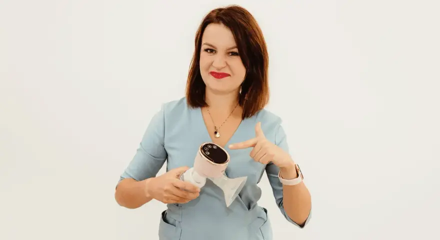 Kobieta w niebieskiej bluzce wskazuje palcem na różowy laktator elektryczny.
