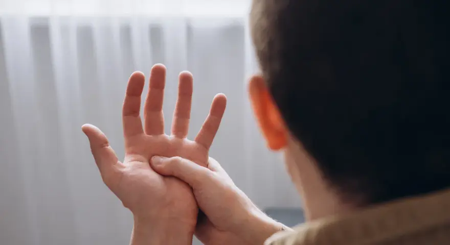Mężczyzna masuje dłoń, odczuwając drętwienie rąk.
