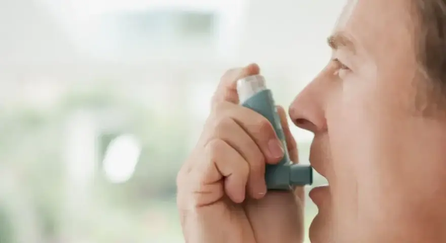 Mężczyzna używa inhalatora benodil, by złagodzić objawy astmy.