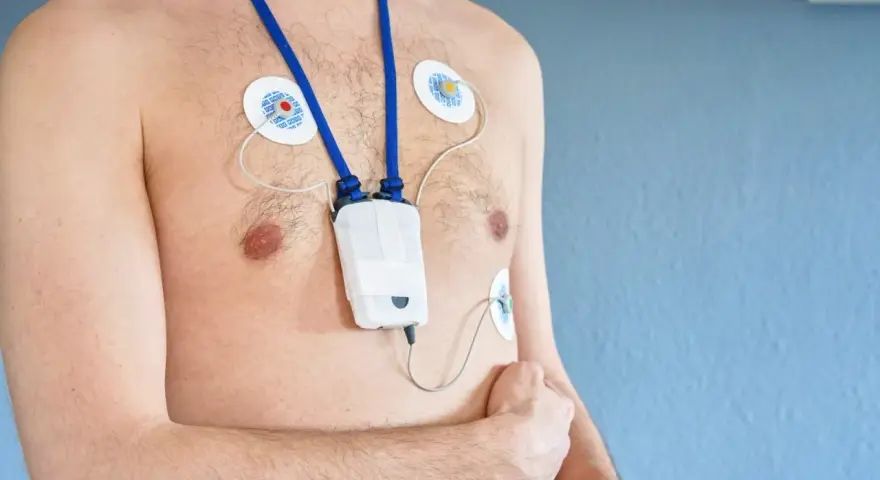 Mężczyzna z przyklejonymi elektrodami i urządzeniem holter ekg na szyi, monitorującym pracę serca.