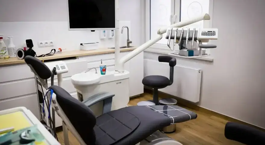 Nowoczesny gabinet stomatologiczny z fotelem, unitem i ekranem.