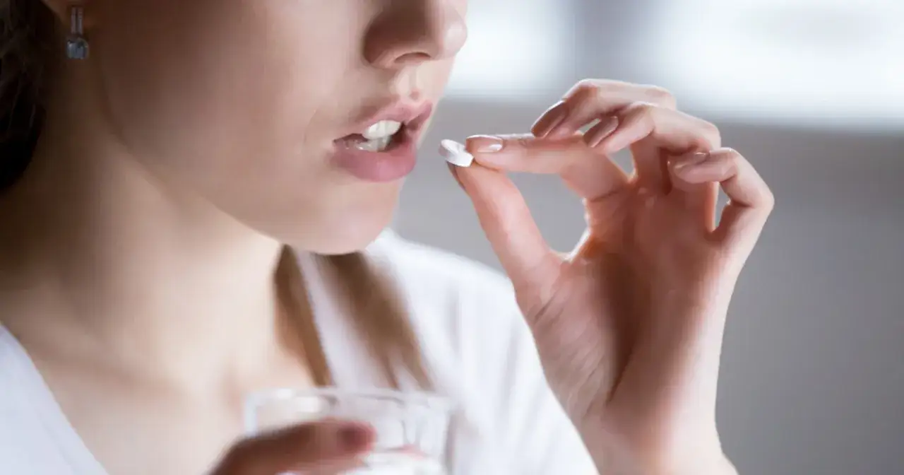 Kobieta bierze tabletkę levofloxacin, trzymając szklankę wody.
