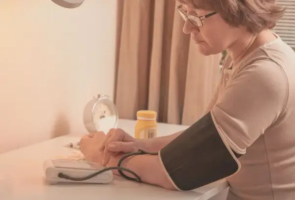 Kobieta w okularach mierzy ciśnienie. Na stole leżą tabletki i budzik. To część jej codziennej rutyny, by dbać o tezeo.