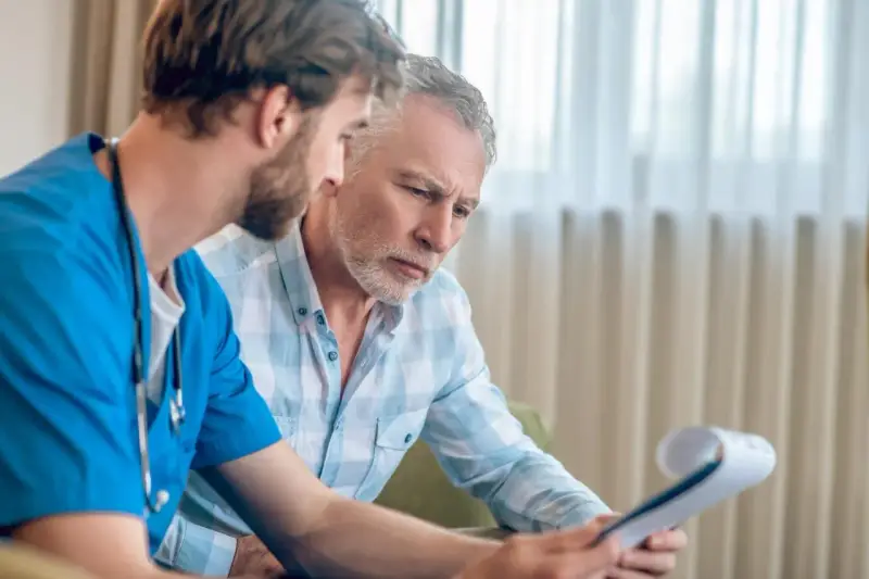 Lekarz w niebieskim fartuchu omawia z pacjentem wyniki badań, prawdopodobnie dotyczące biopsji prostaty.